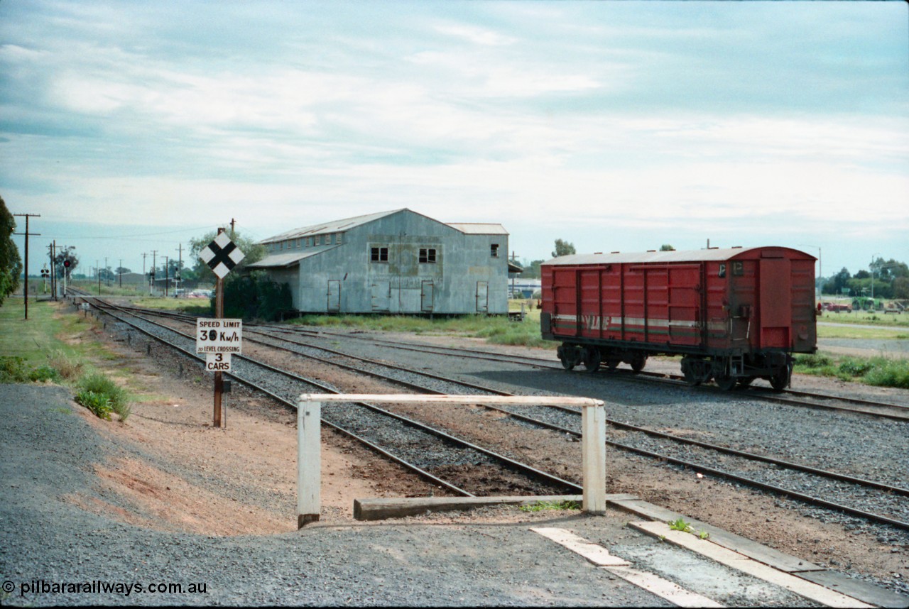 161-19
Cobram, station yard overview looking south from the platform, searchlight signal post and grade crossing with speed board and indicator, corrugated iron shed, V/Line broad gauge D type bogie louvre van in yard having being shunted off an earlier down passenger train.
