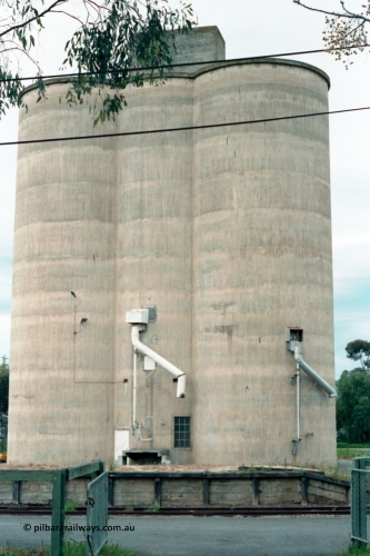 161-03
Numurkah, view from outside platform looking across yard through gates, goods loading platform visible with Williamstown style silo complex located behind it with train loading spouts.
