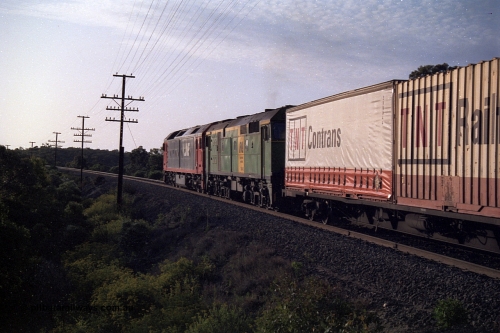 168-10
Bank Box Loop, trailing view of down V/Line broad gauge goods train to Adelaide with G class G 540 Clyde Engineering EMD model JT26C-2SS serial 89-1273 and Australian National 700 class 704 AE Goodwin ALCo model DL500G serial G6059-2 power away from the crossing loop at the Ironbark Road grade crossing.
