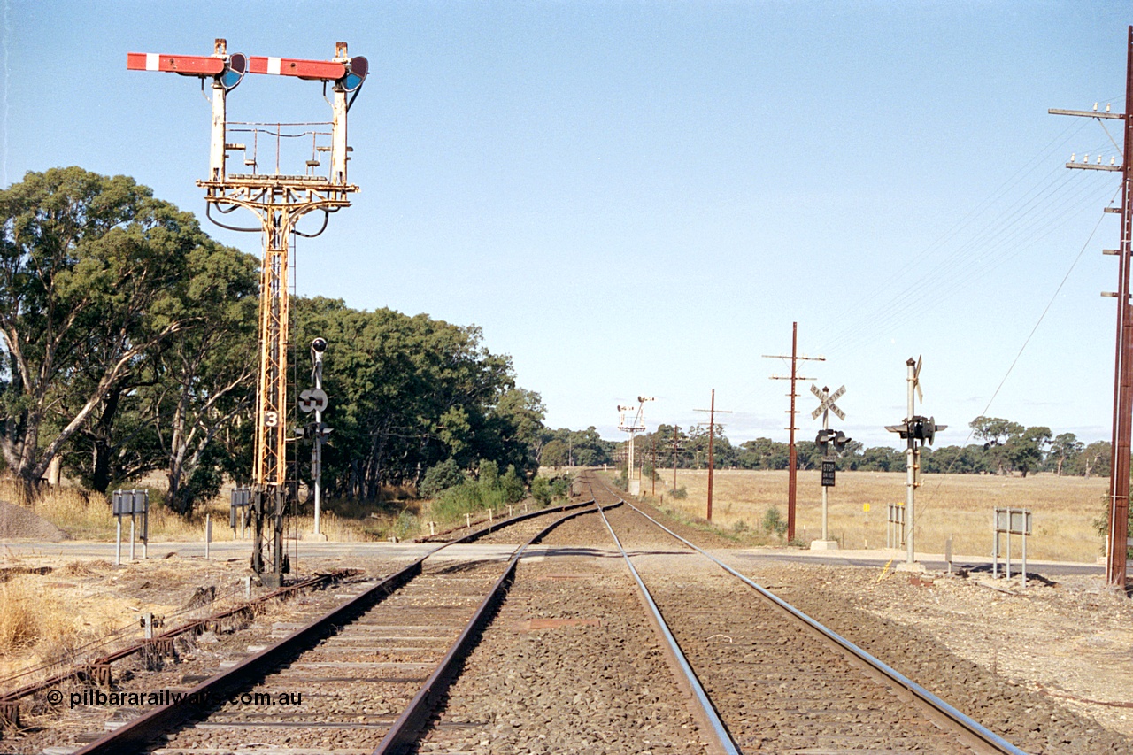171-17
Buangor station yard overview, looking towards Melbourne, east end of loop, up home semaphore signal Post 3, point rodding and signal wires, High Street grade crossing and semaphore signal Post 2 facing down trains in the distance.
