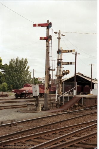 172-37
Ballarat station yard, platform, wooden semaphore signal post 21 facing camera and 21B at platform one facing away, Tait carriages and VZBF class bogie brake block transport waggon in background. Post 21 top is the Down Home No.1 to Post 26, bottom is the Calling On to No. 1. Post 21B top is Up Home No. 1 to Post 7, bottom is Up Home No.1 to No.1 A to Post 9B. Left disc is No.1 to Goods Line via 'Z' to Post 7. Right disc is from No.1 to Loco Track Post 10 or Goods Track 'R'.
