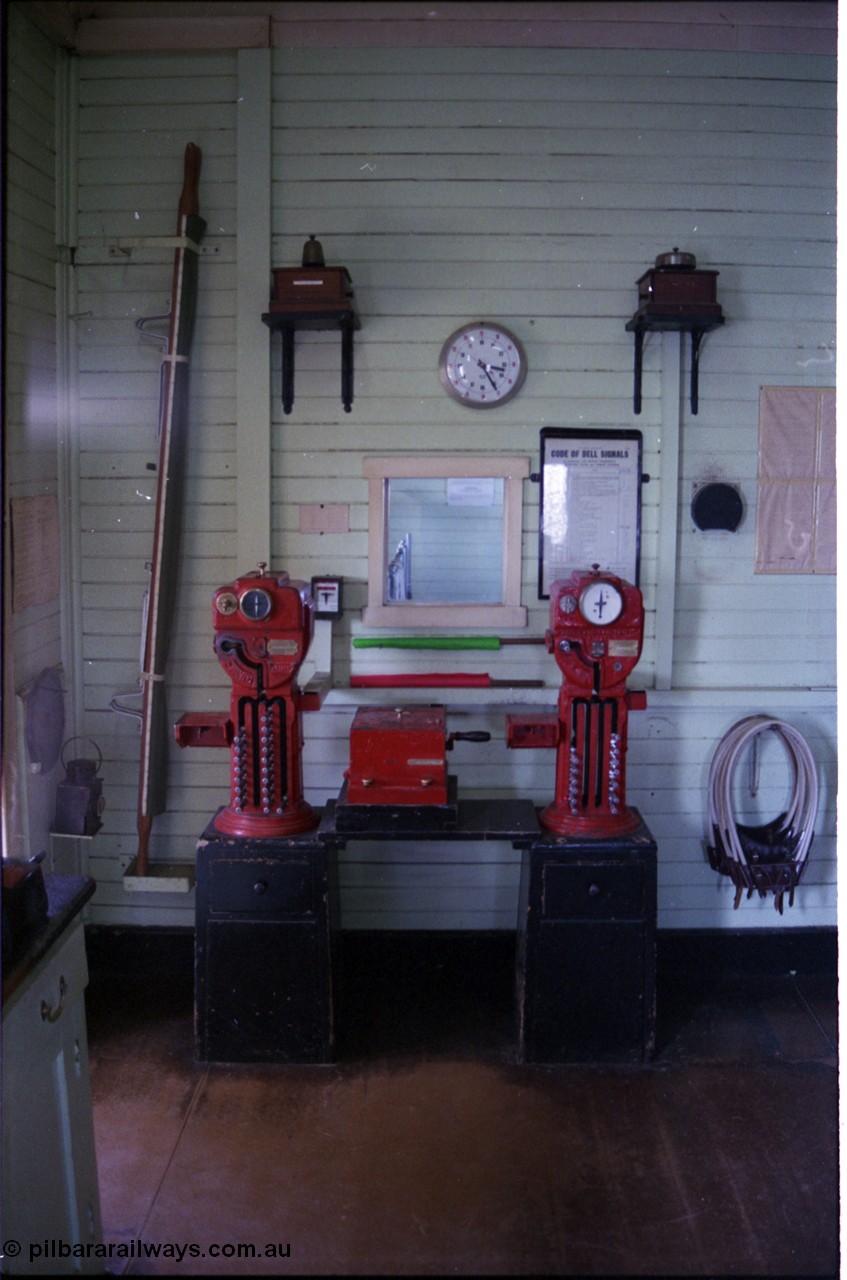 179-32
Gheringhap, internal view of signal box showing the electric staff instruments for the North Geelong C section on the left and the Meredith section on the right, above each exchanger is the respective bell for each section, along with wall clock and Code of Bell Signals wall chart, to left is a station stretcher and hand lamp and on the right the electric staff carriers or hoops. At the very left of frame the train register desk can be just seen, through the opening in the wall behind the exchangers can be seen the 18+2 lever frame levers.
