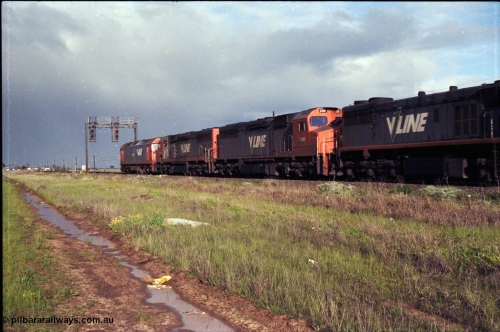 183-03
Deer Park West, an up broad gauge V/Line goods train behind the quad lash up of a G class, 2 C classes and an X class as they pass under signal gantry with searchlight signals 1/10 and 1/22 on the North Line.
